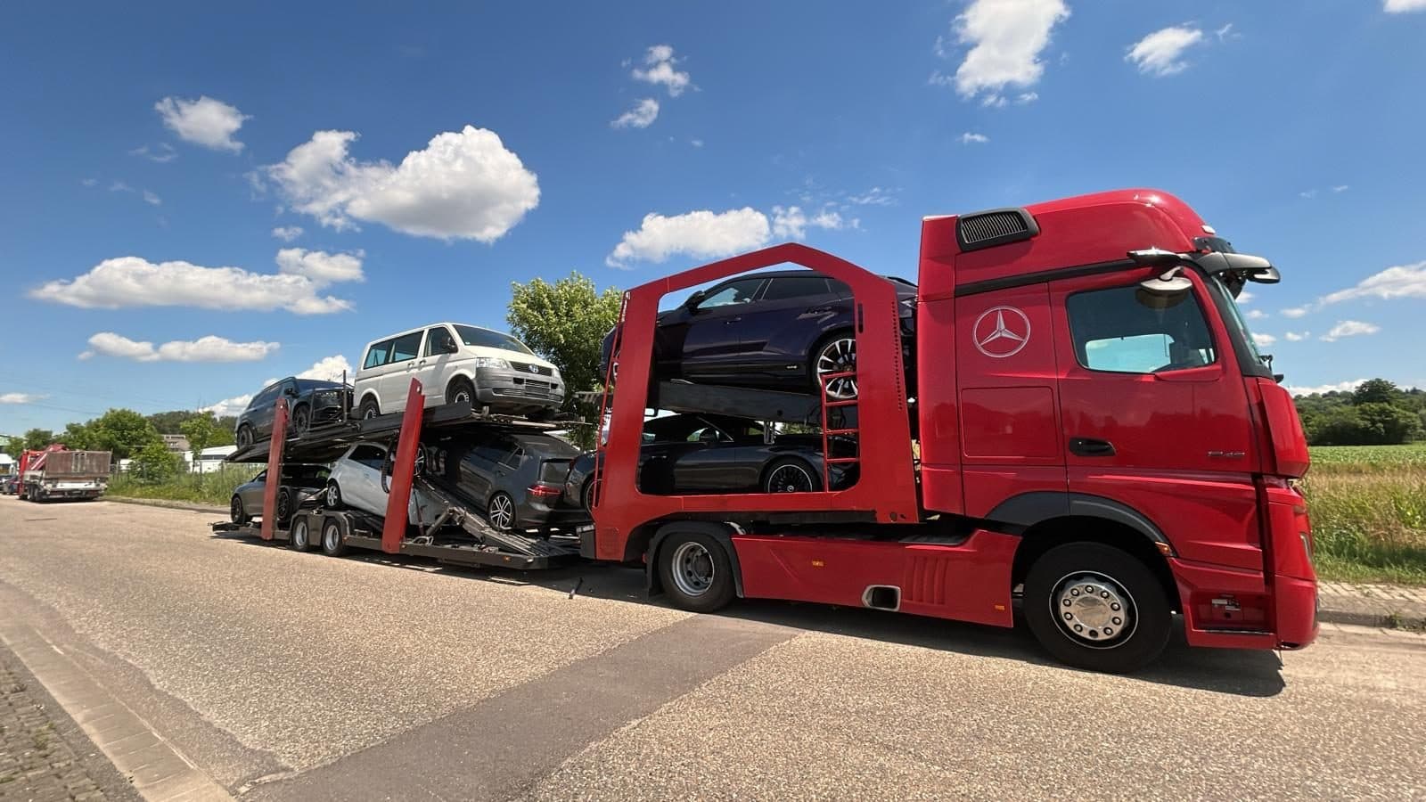 Czerwony autotransporter z samochodami na dwóch poziomach pod błękitnym niebem